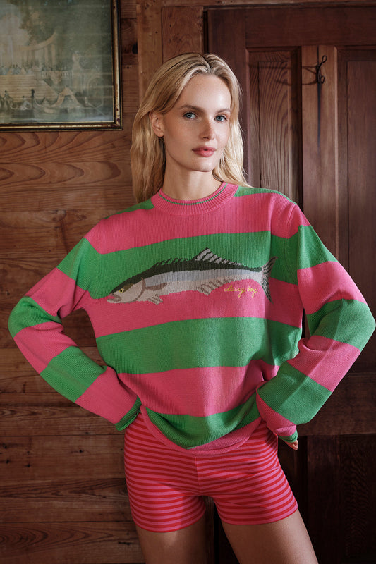 Woman wearing a pink and green striped sweater with a fish design in a wooden interior setting. |M1