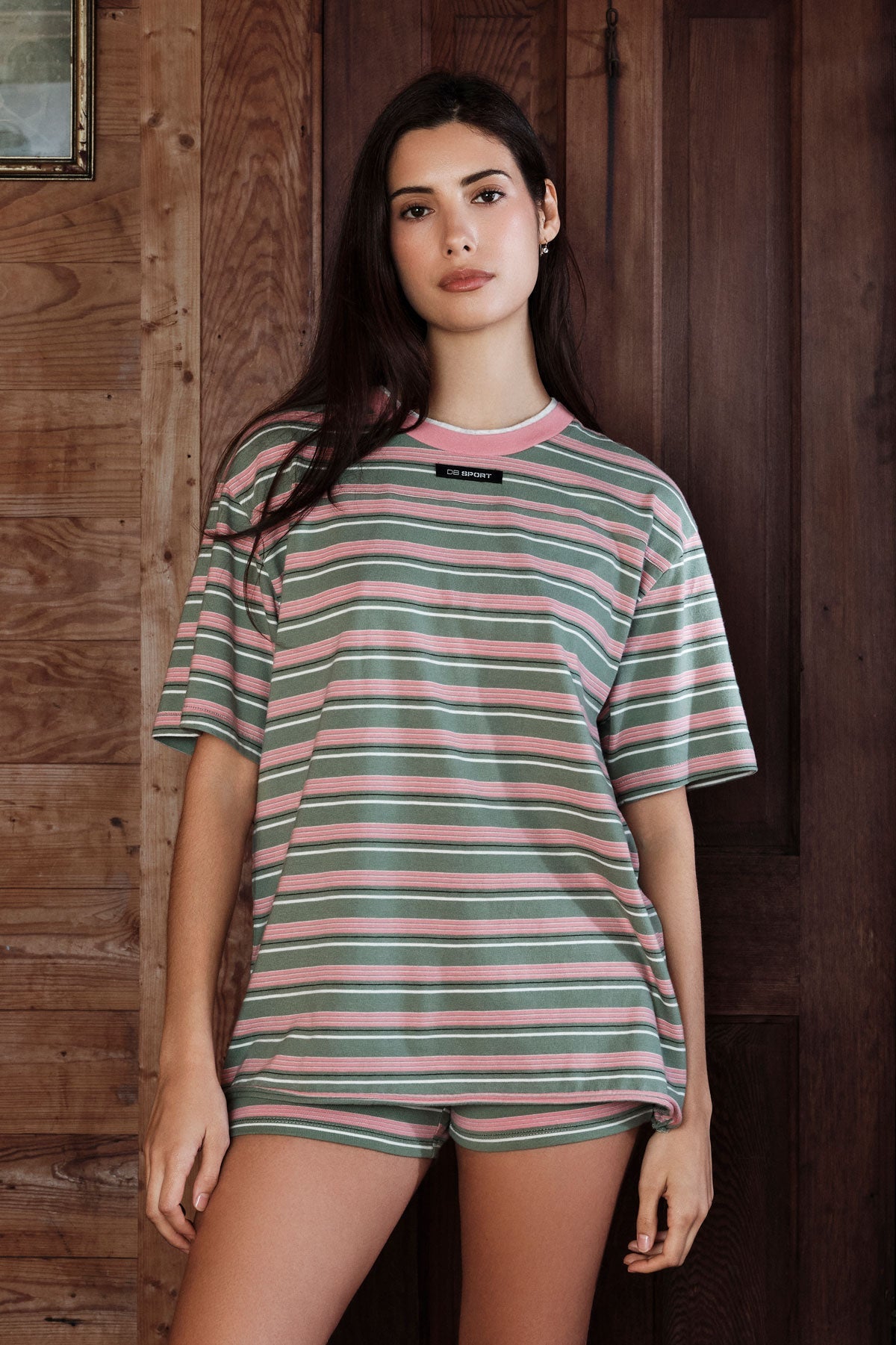 Woman wearing a striped shirt and shorts in front of a wooden wall |M1
